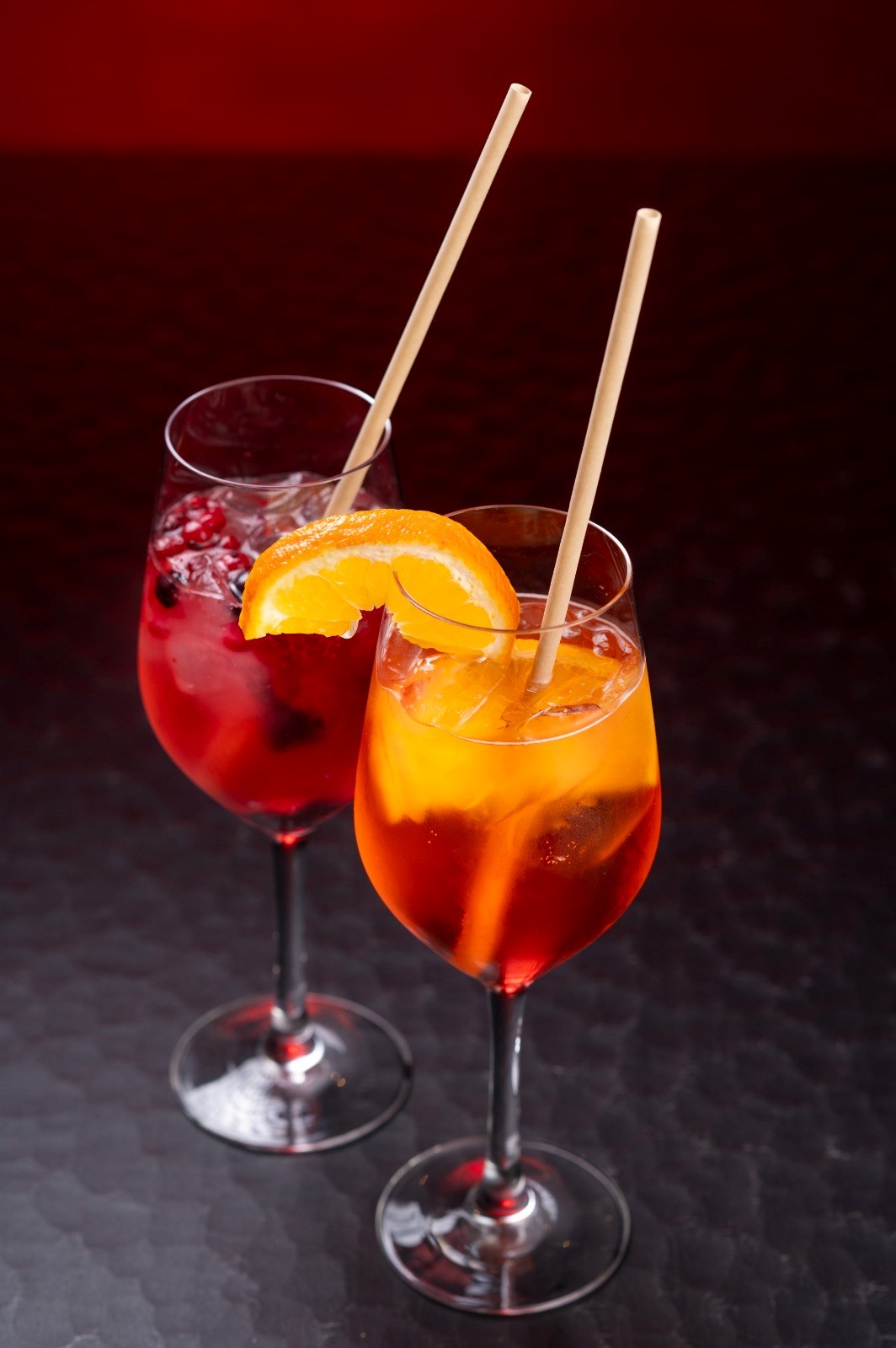 Zwei Gläser mit Aperitif-Cocktails, Orangenscheibe, Röhrchen, roter und orangefarbener Drink.