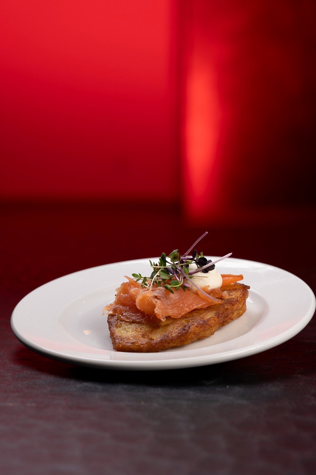 Ein Teller mit geröstetem Brot, belegt mit Lachs, Sahne und Kräutern vor rotem Hintergrund.