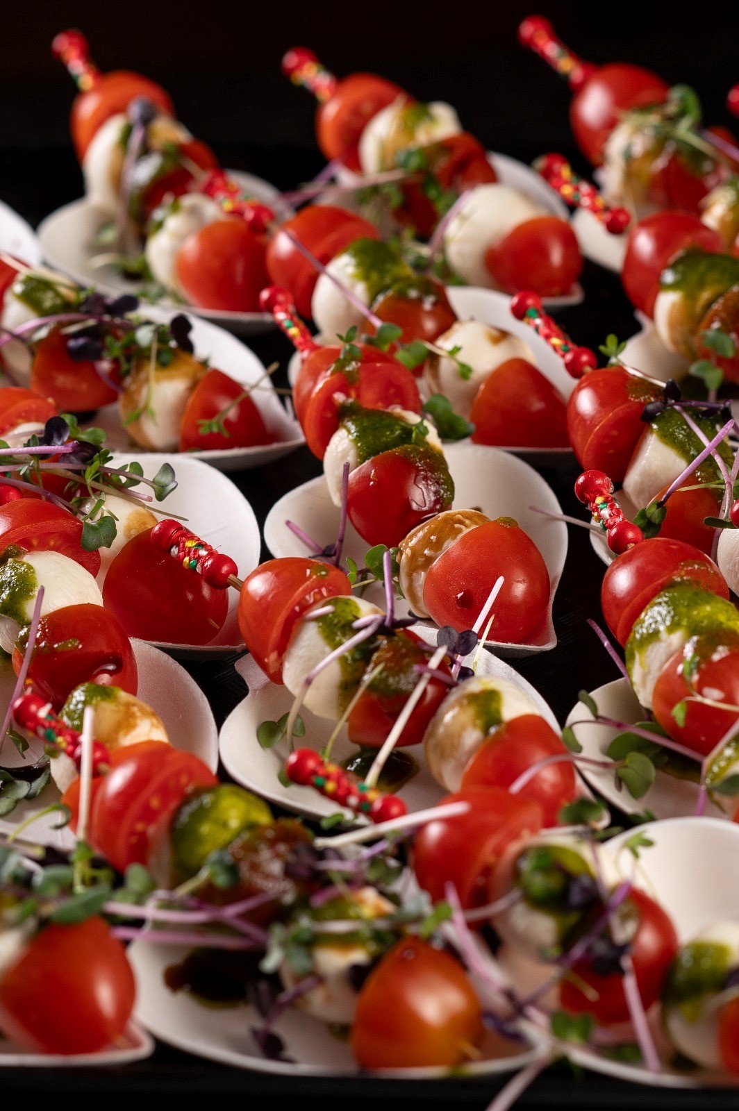 Caprese-Spieße mit Kirschtomaten, Mozzarella, Basilikum, Balsamico und Mikrogrün auf weißem Teller.