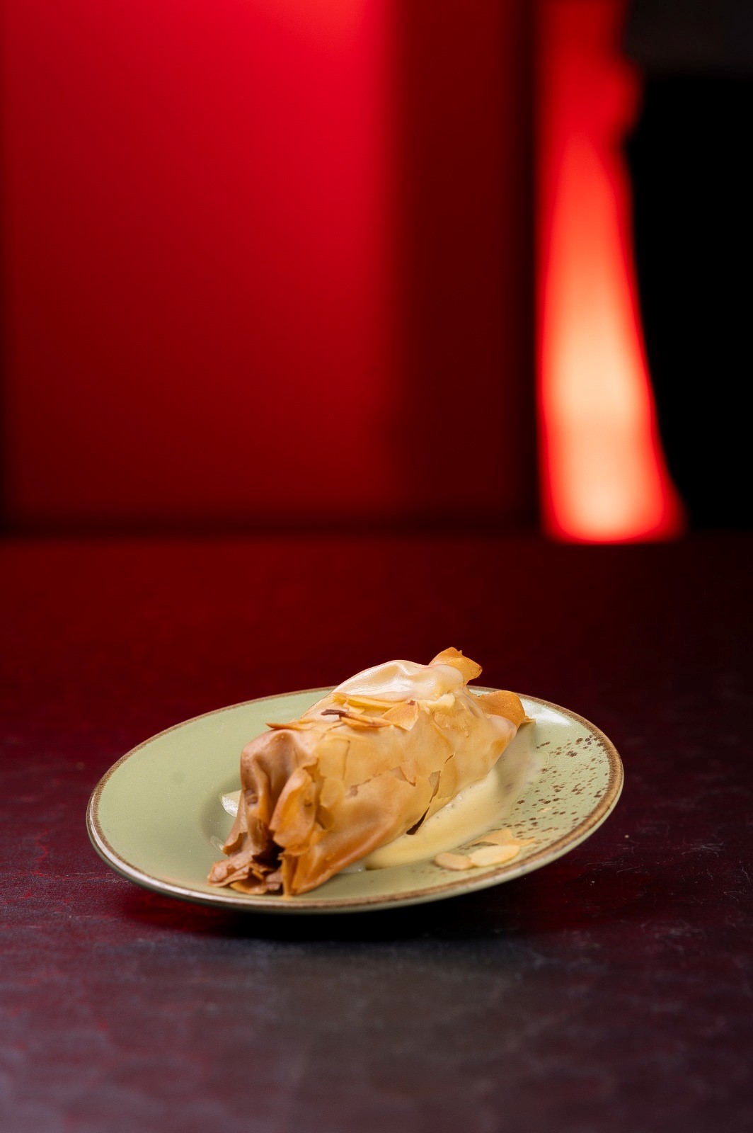 Ein Strudel auf grünem Teller, knusprig braun, auf schwarzem Tisch mit rotem Hintergrund.