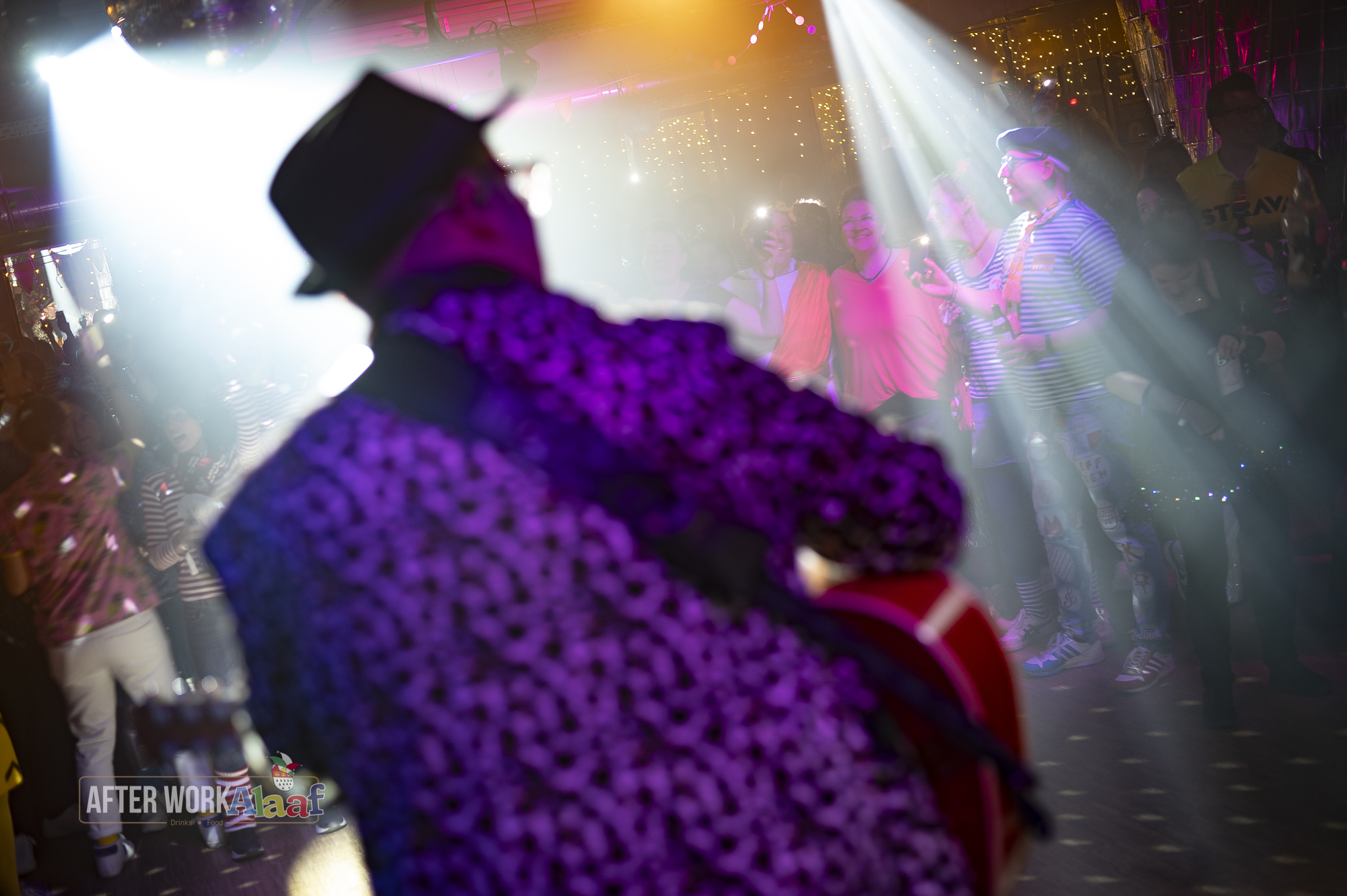 Ein Musiker mit Hut spielt Gitarre vor fröhlichem Publikum im bunten Lichtstrahl