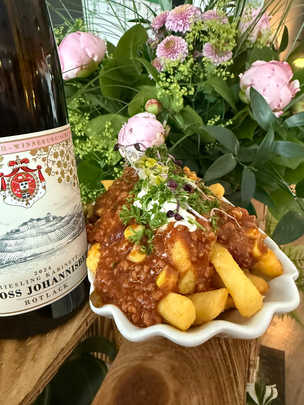 Eine Schale Pommes mit Chili, Sauerrahm und Kräutern neben einer Flasche Weißwein