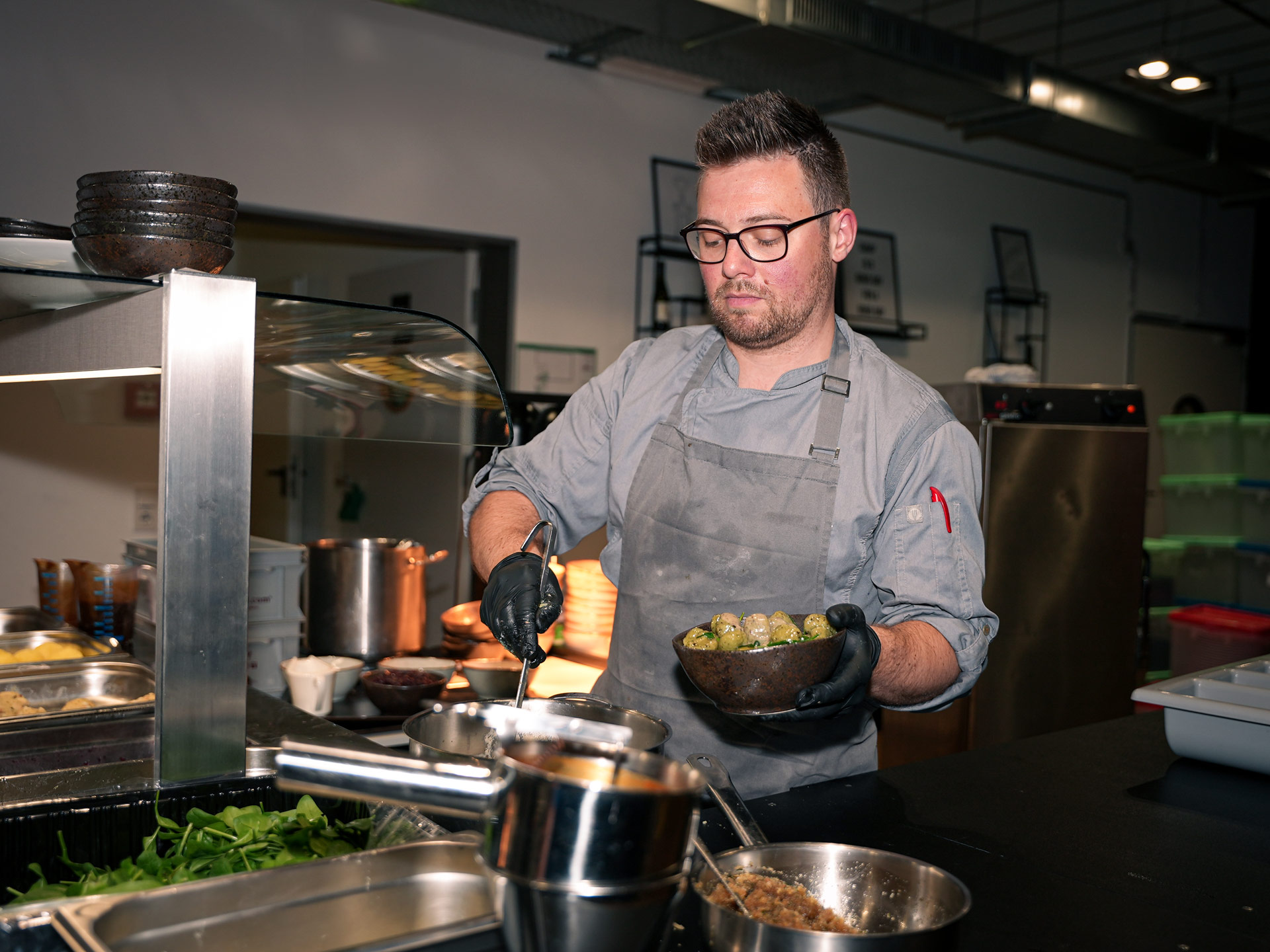 Ein Mann mit Brille und Bart serviert konzentriert Essen in einer modernen Küche