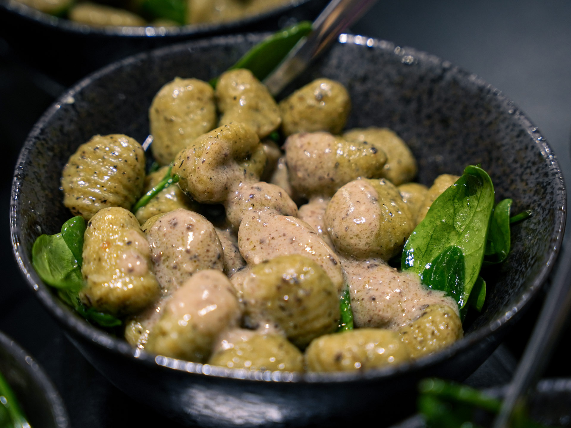 Grüne Gnocchi mit cremiger heller Sauce und frischem Spinat in einer dunklen Schüssel
