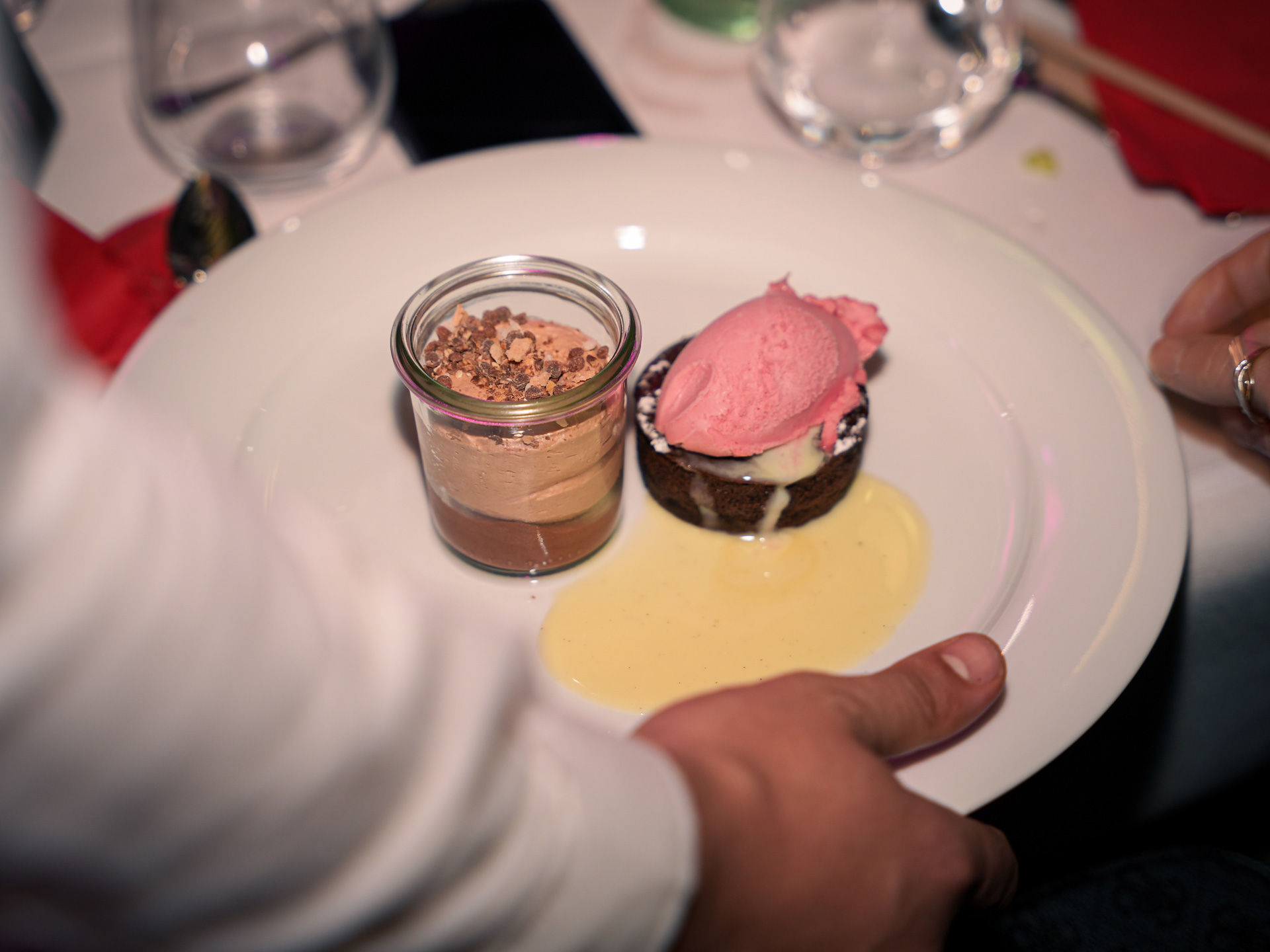 Eine Person hält einen Teller mit einem Dessert im Glas und Schokoladenkuchen mit Eis