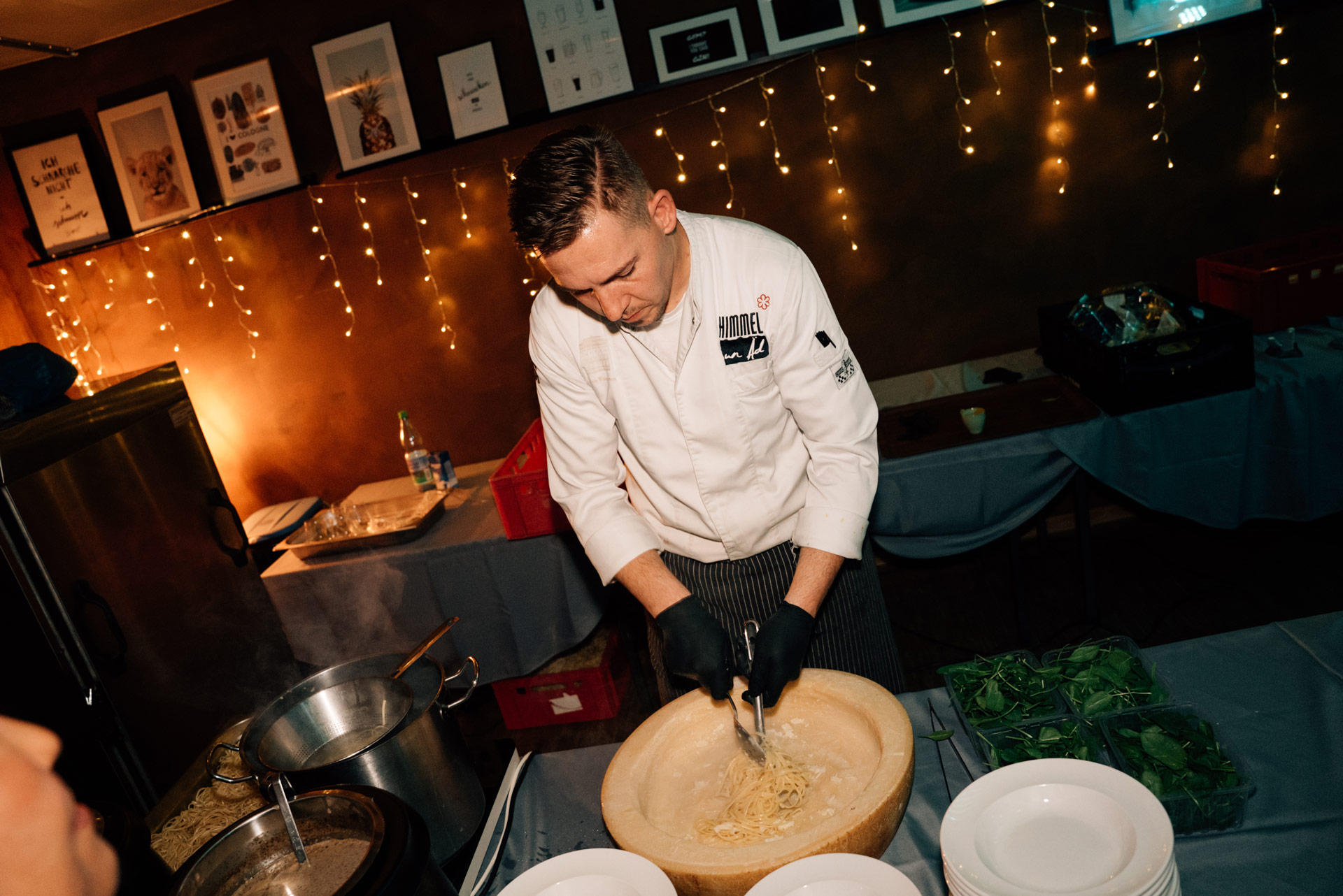 Ein Koch mit konzentriertem Blick serviert Pasta aus einem großen Käselaib unter Lichterketten
