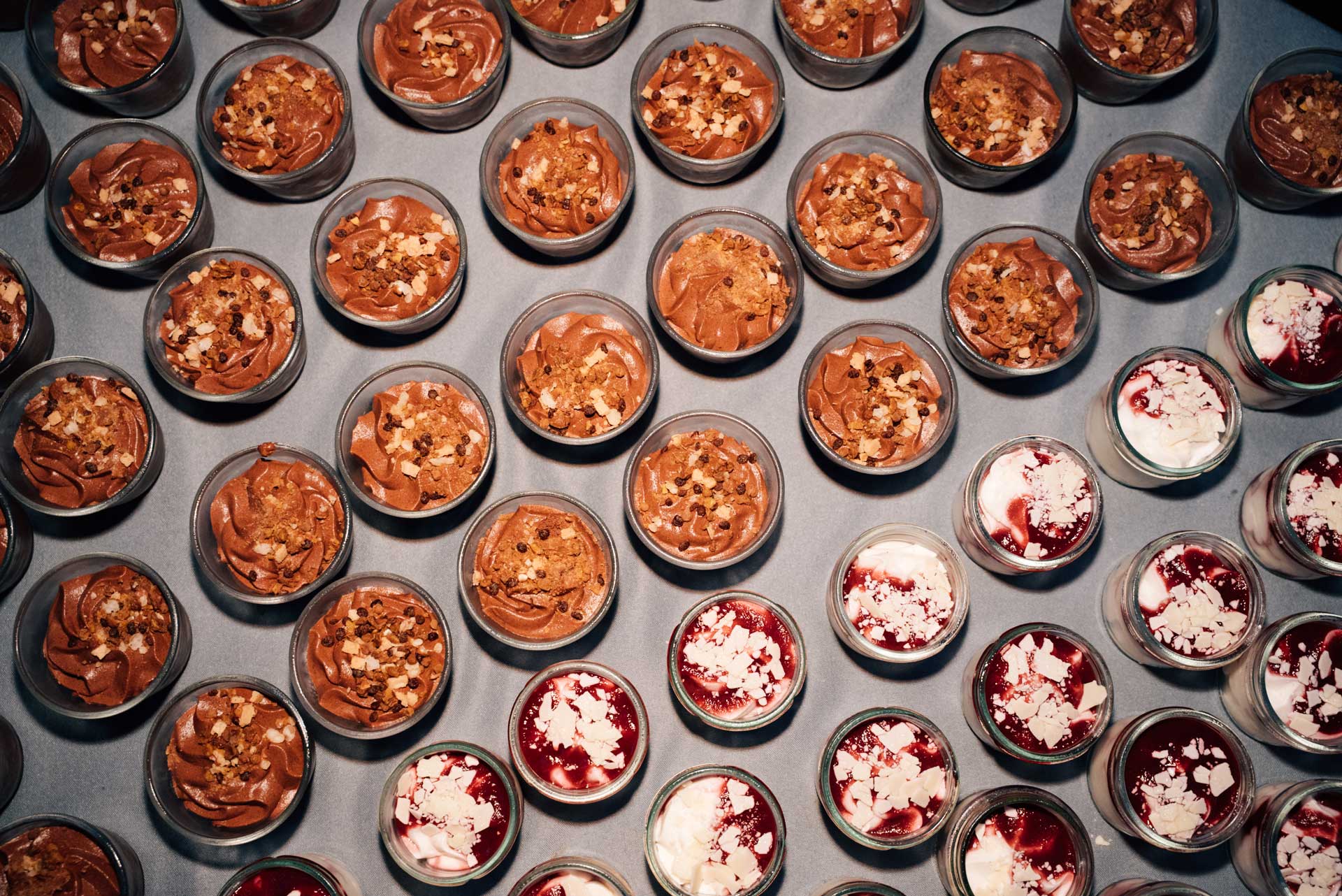 Viele Gläser mit Schokoladen- und Frucht-Desserts in unterschiedlichen Farben