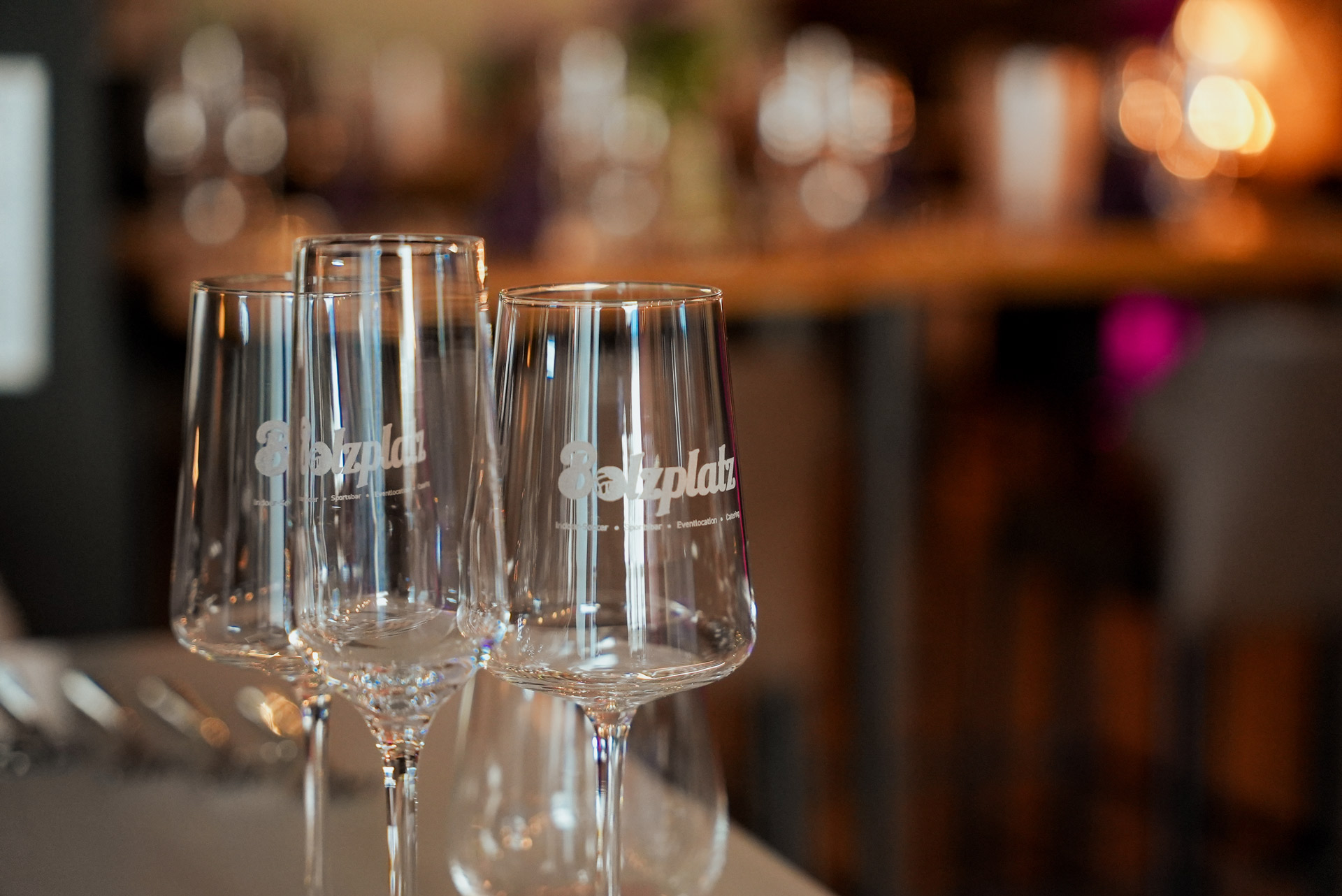 Drei leere Weingläser mit Gravur stehen auf einem Tisch in stimmungsvoller Beleuchtung