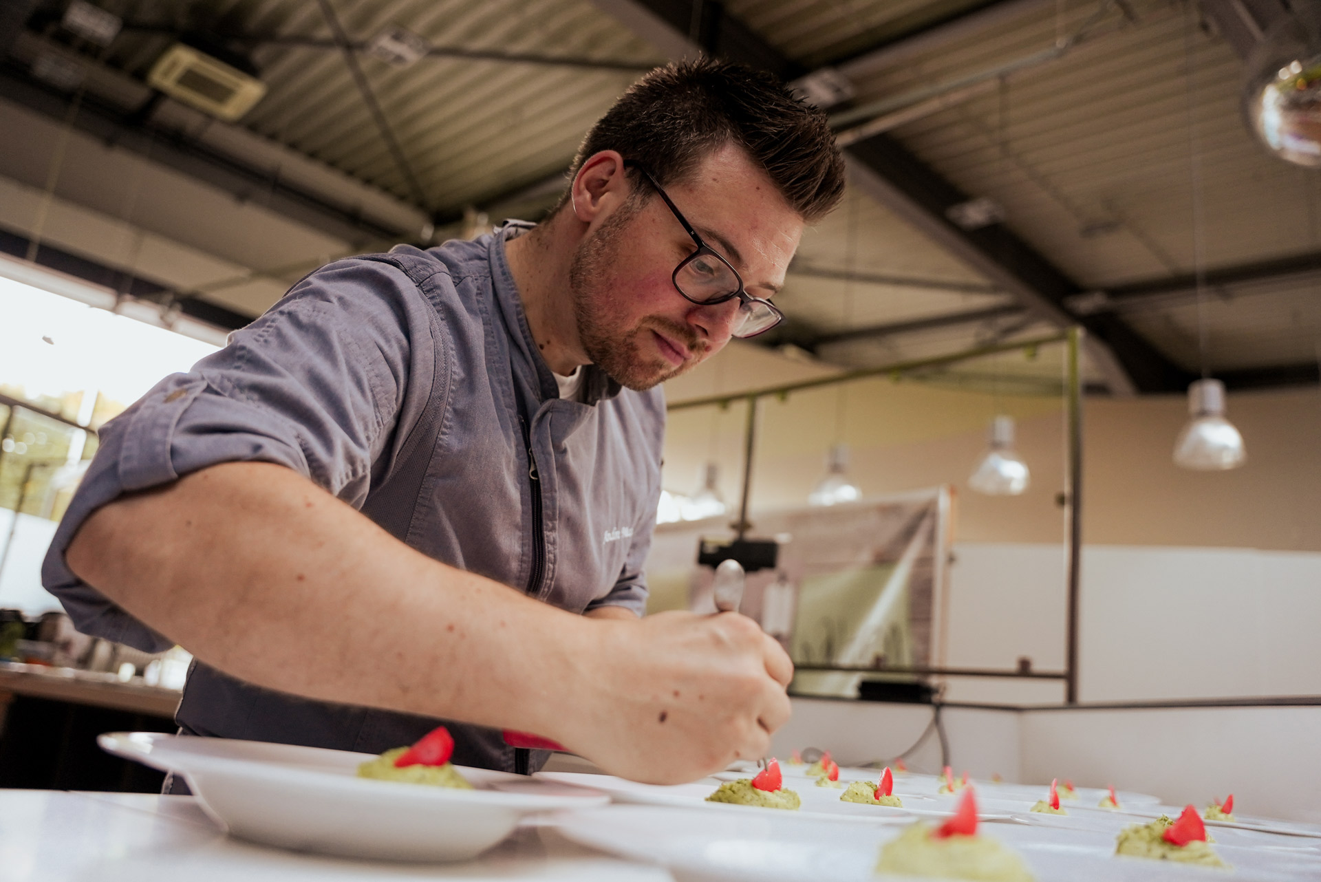 Ein Mann mit Brille und Bart dekoriert konzentriert kleine grüne Speisen mit Rot