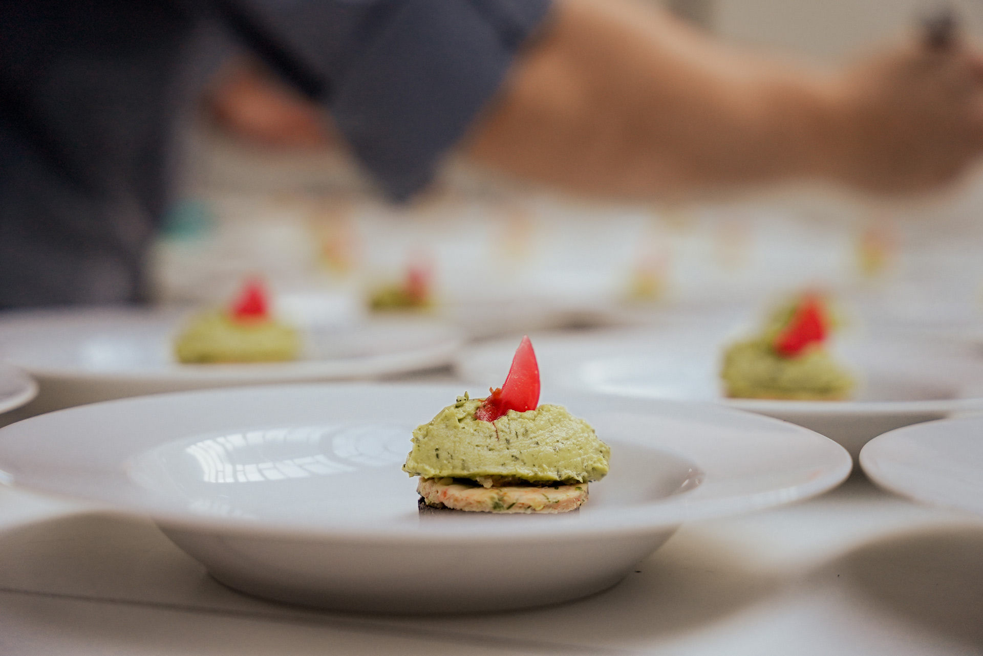 Eine unbekannte Person richtet konzentriert ein kleines grünes Häppchen mit rotem Topping an