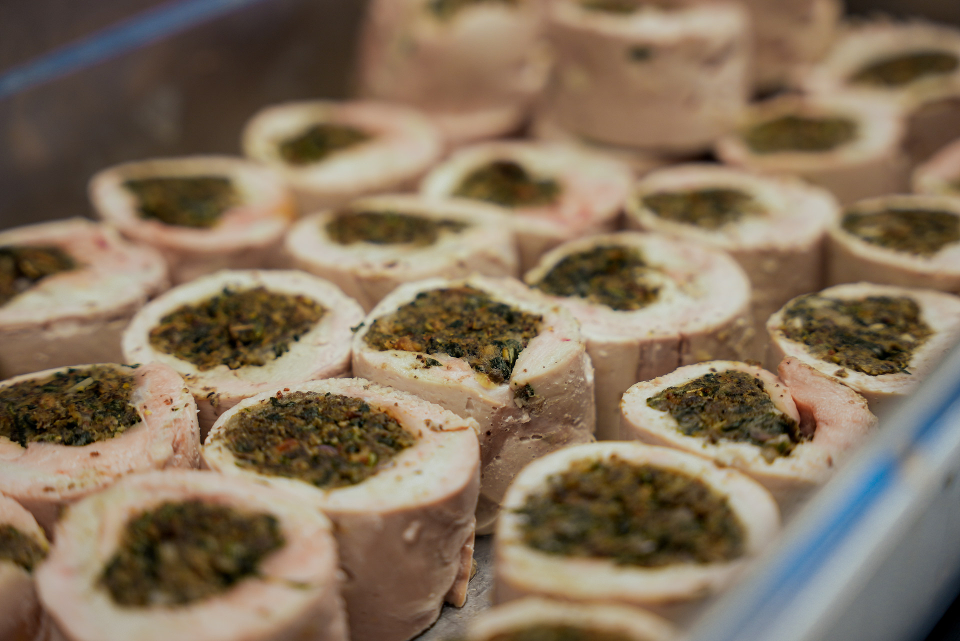 Mehrere aufgeschnittene Rouladen aus hellem Fleisch mit grüner Kräuterfüllung