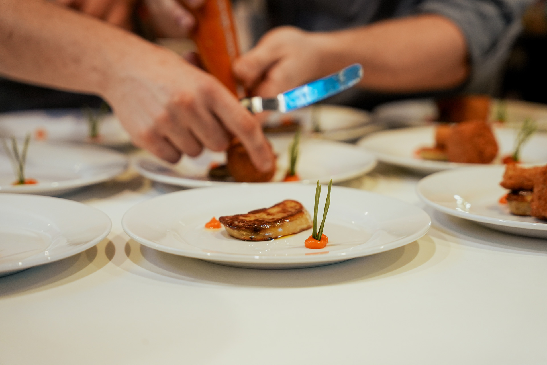 Zwei Personen richten konzentriert ein gebräuntes Gourmetgericht kunstvoll mit Messer und Garnitur an