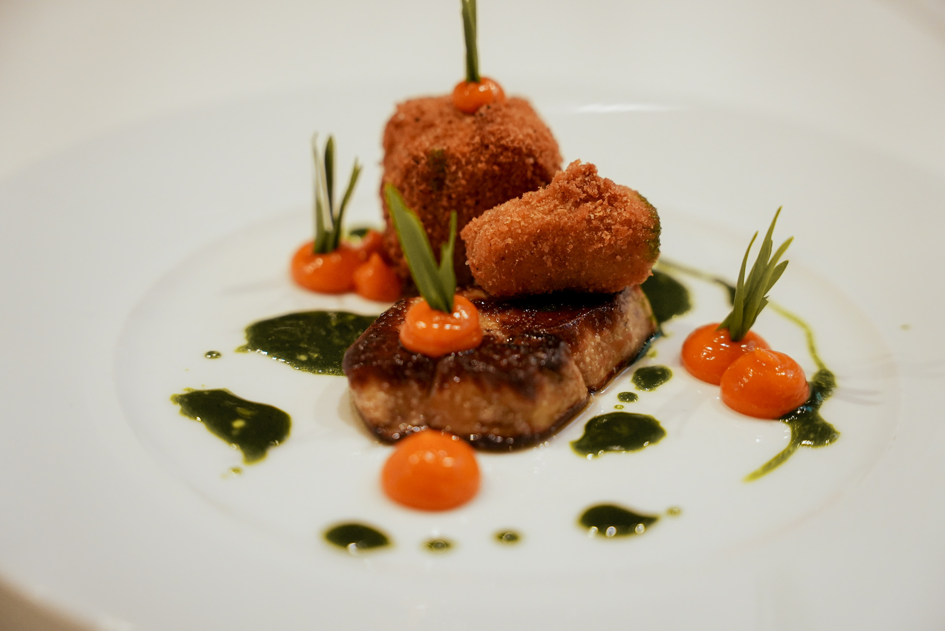 Gebratenes Fleischstück mit knusprigen Bällchen, grüner Sauce und orangefarbenen Tupfern kunstvoll angerichtet