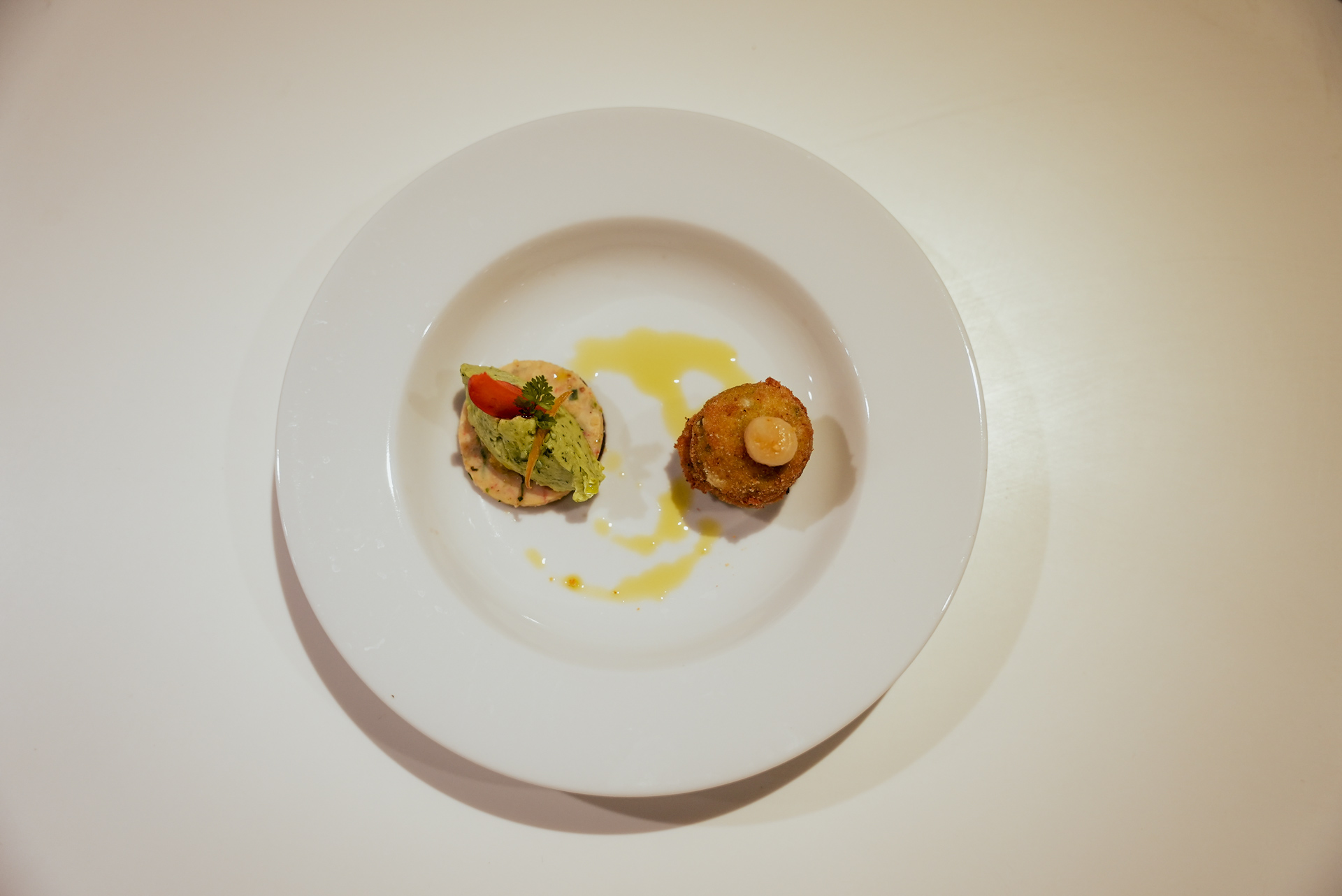 Ein weißer Teller mit zwei raffinierten Häppchen, garniert mit grünen und roten Akzenten