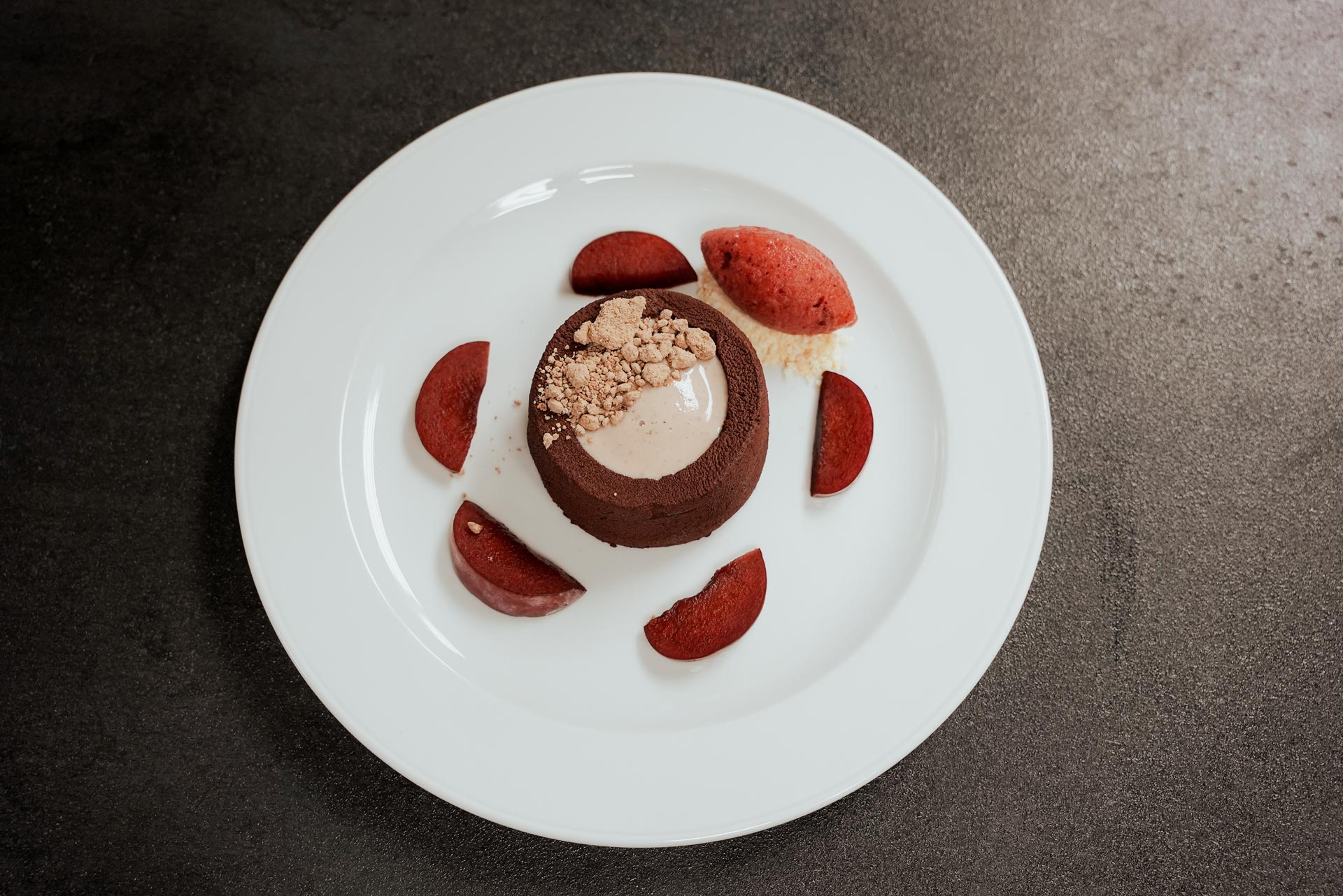 Ein dunkles Schokoladendessert mit heller Creme und Pflaumen auf weißem Teller